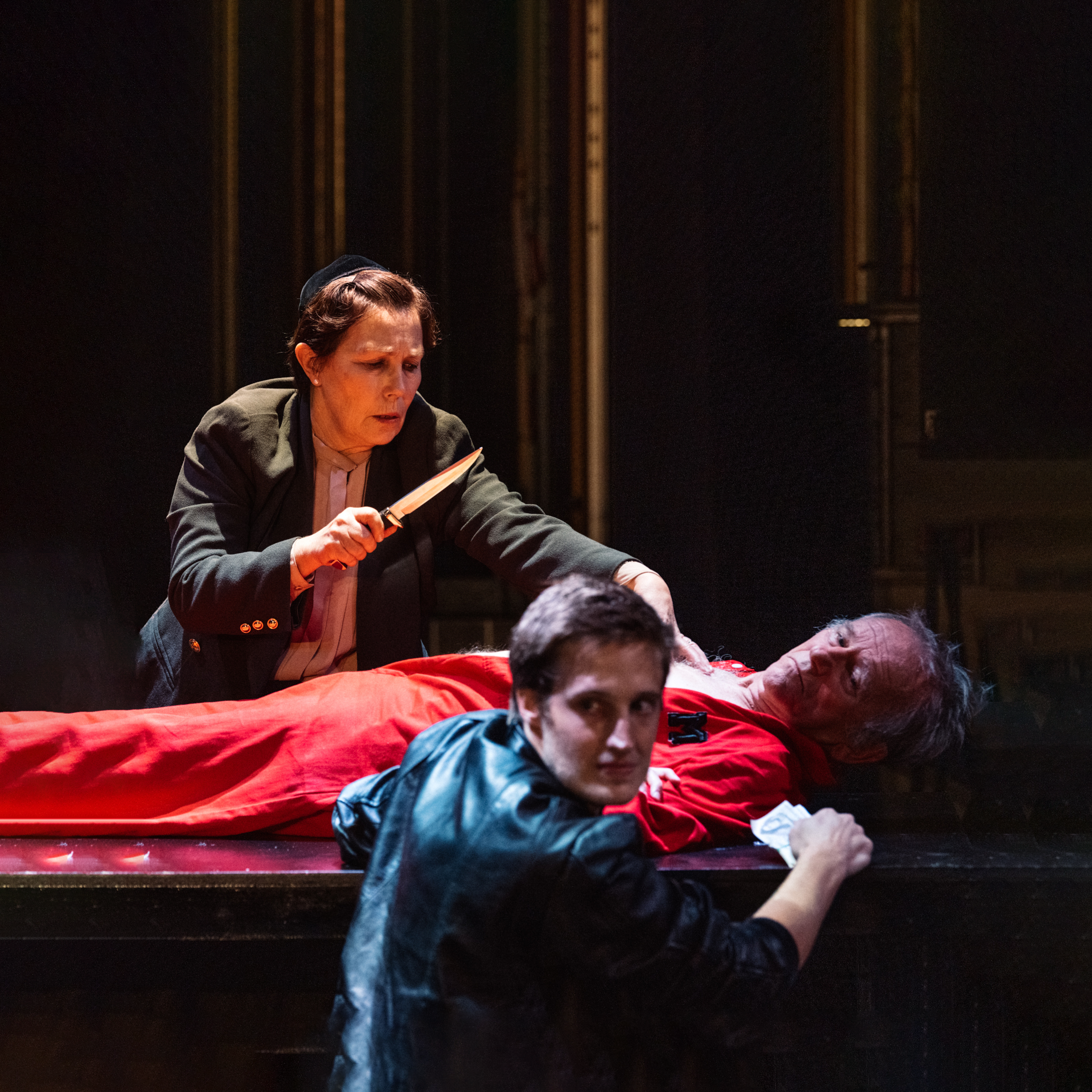Promotional image of The Merchant Of Venice Symposium for Seymour Centres Arts Education Program depicting a man lying on a bed with a woman standing over holding a knife, a boy sits in the foreground looking past the camera.