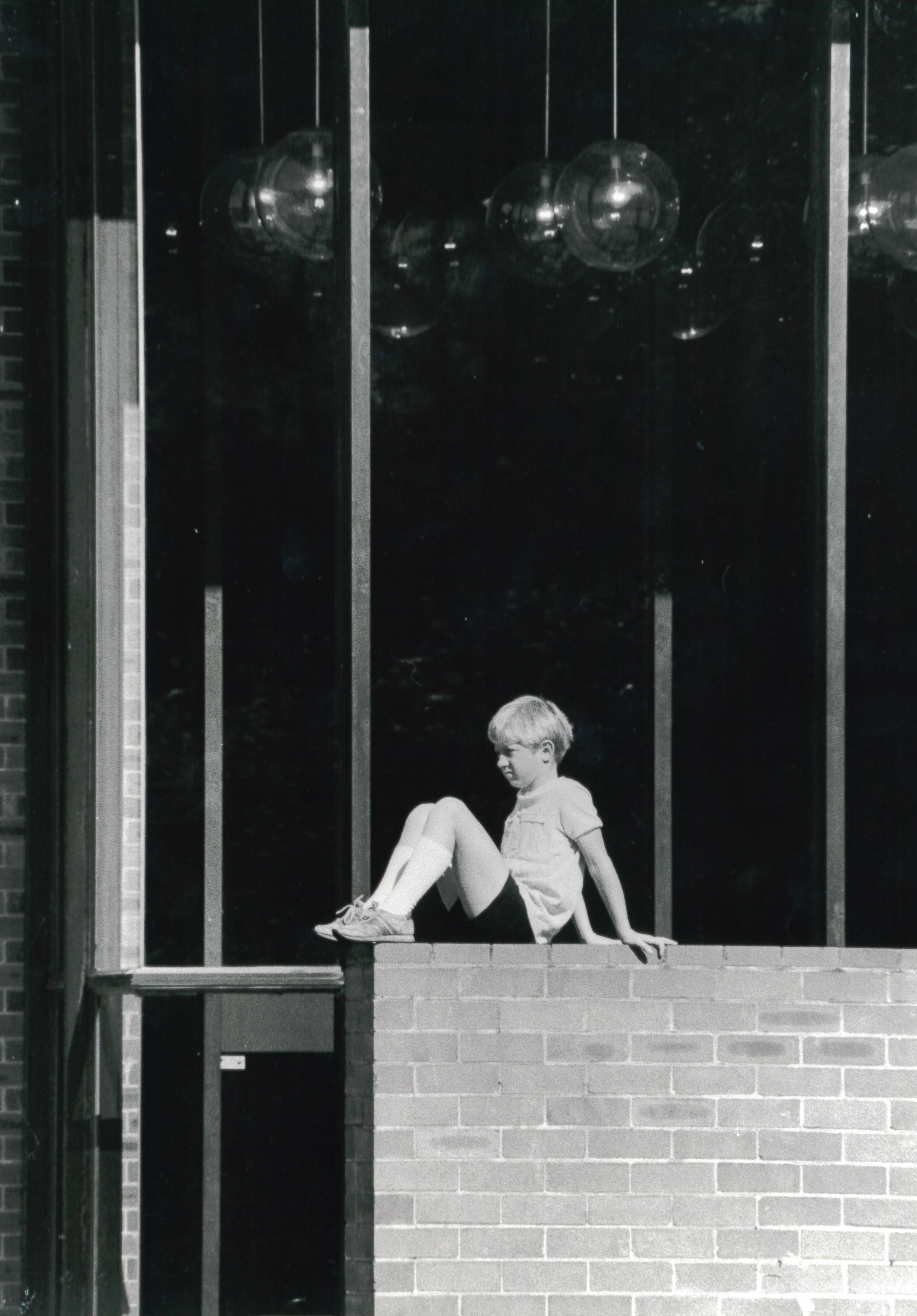 Black and white archival image of a Sydney Youth Theatre Festival in 1985 perched on a brick wall outside of the Seymour Centre.