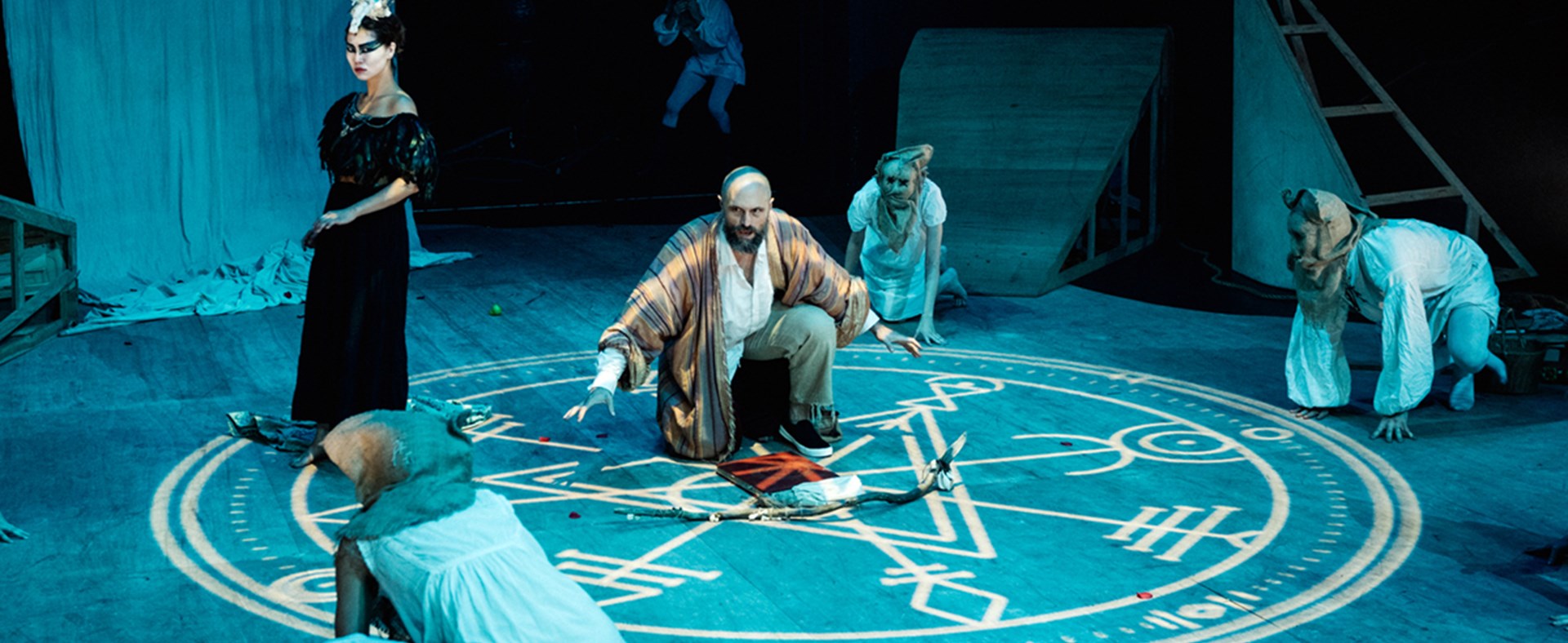 Image of the Tempest/Hag-seed Symposium by Sport For Jove Theatre Company. Shows five actors in the foreground crouching around a projected circle with symbols on the floor.