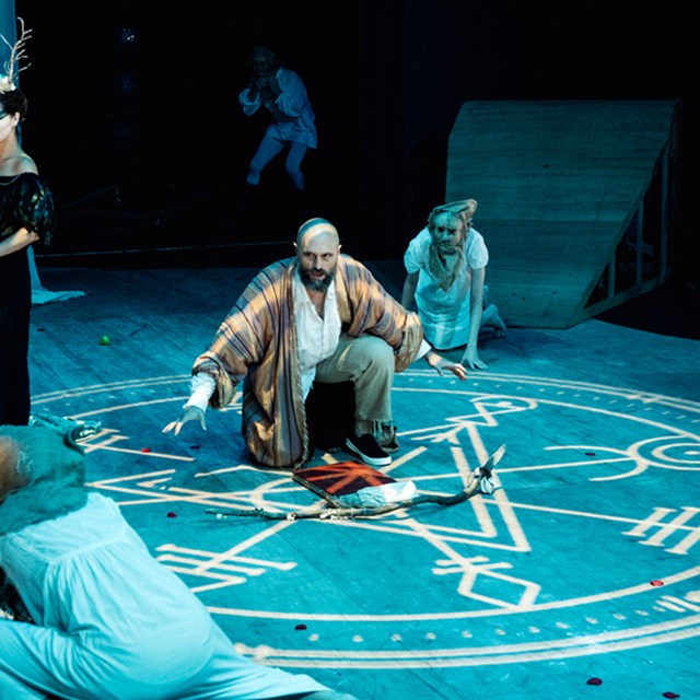 Image of the Tempest/Hag-seed Symposium by Sport For Jove Theatre Company. Shows five actors in the foreground crouching around a projected circle with symbols on the floor.