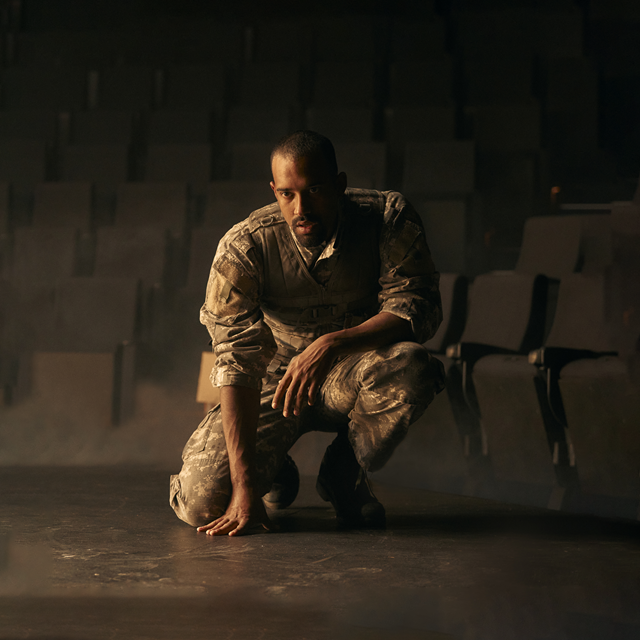 Promotional image of Othello Symposium for Seymour Centres Arts Education Program depicting a man in camouflage army uniform crouching and looking past the camera.