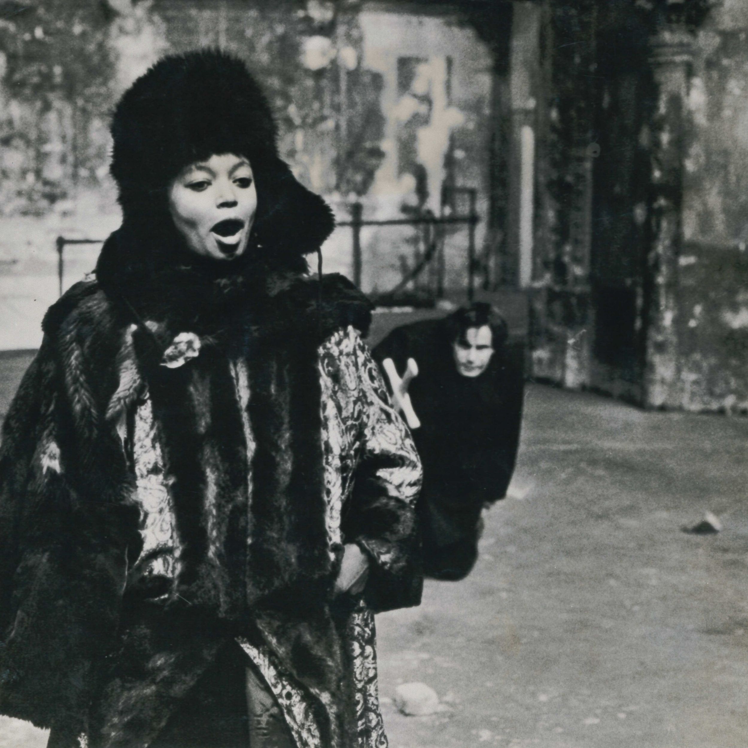 Black and white archival image of two actors, the female actor in the foreground singing and the male actor in the background creeping up behind.