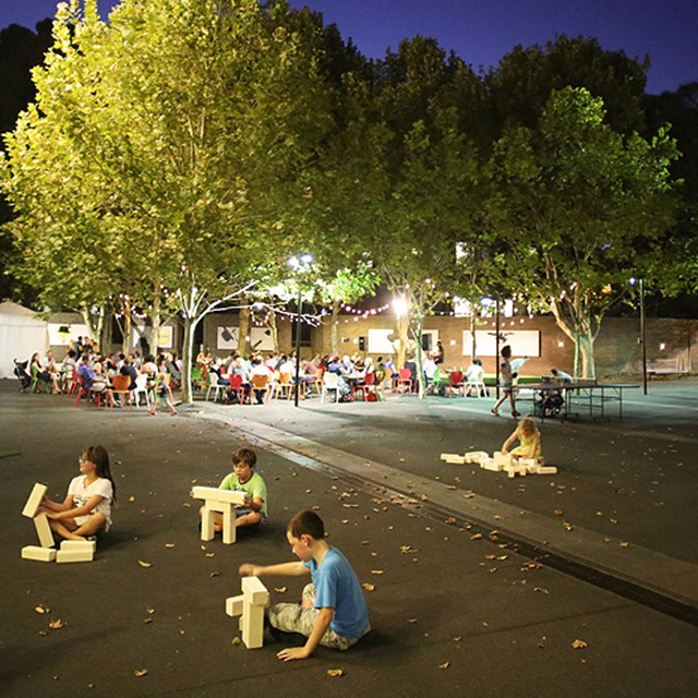 Children playing with building blocks in outdoor courtyard event space at night.