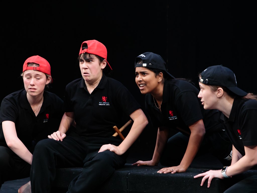 4 school students making faces in drama class sitting on a black box.