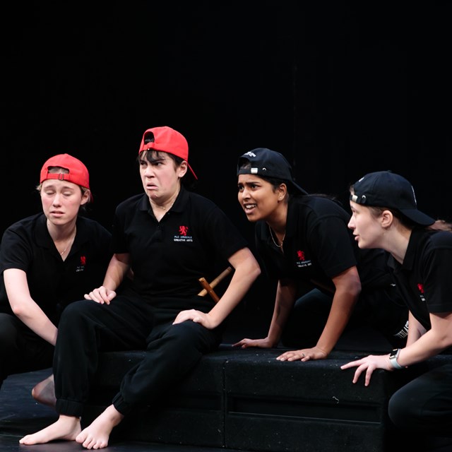 4 school students making faces in drama class sitting on a black box.