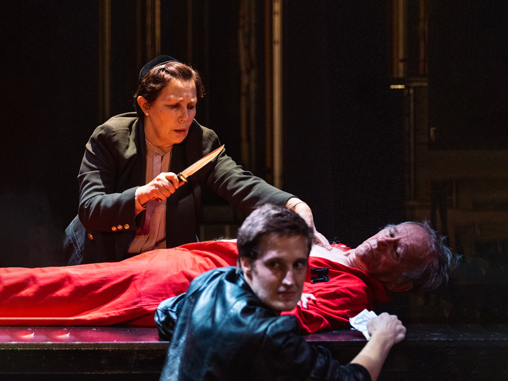 Promotional image of The Merchant Of Venice Symposium for Seymour Centres Arts Education Program depicting a man lying on a bed with a woman standing over holding a knife, a boy sits in the foreground looking past the camera.