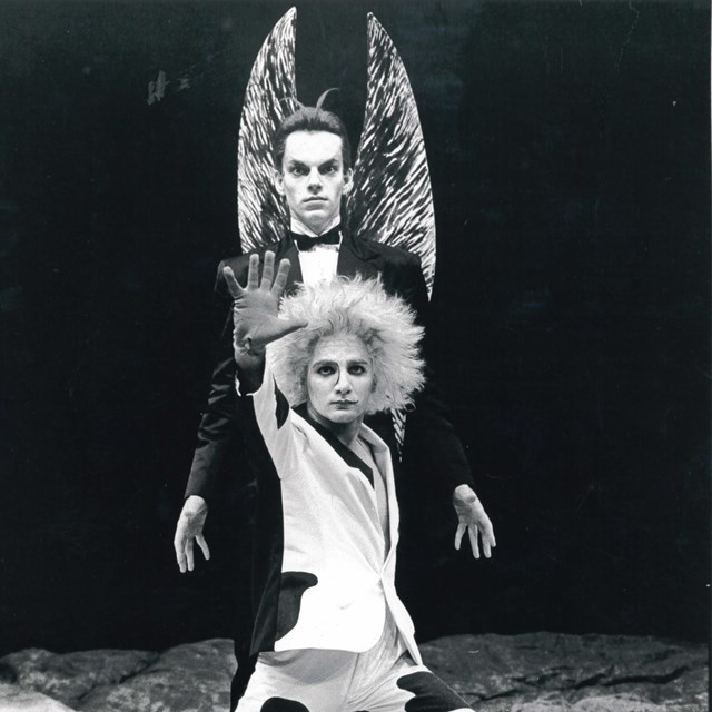 Black and white archival image of Hugo Weaving and Arky Michael Nimrod from 1985. Image shows the actors in full costume and makeup with one crouched infront and the other standing behind, looking out to the audience with intensity.